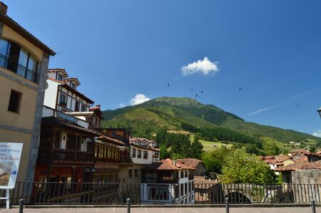 Nice Photo From The Roman Bridge With Buildings In The Foreground And In The Background The Peaks Of Europe In The Villa De Potes. Nature, Architecture, Travel. July 30, 2018. Potes, Cantabria, Spainのeditorial素材
