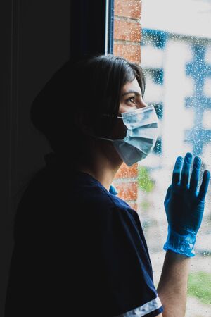 Nurse with face mask in hospital window during pandemic, COVID19の写真素材