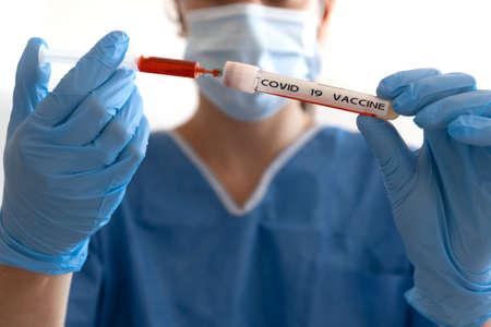 Doctor or nurse with the Covid-19 vaccine holding it in their hands with nitrile glovesの写真素材