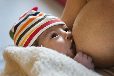 Closeup of a newborn nursing with a striped mesh hat