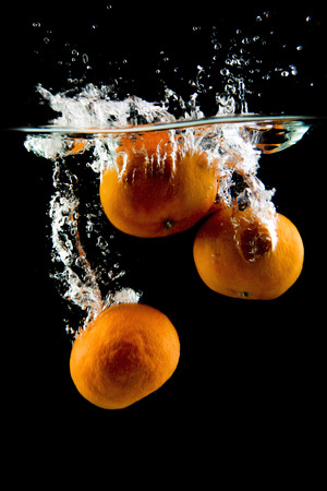 tangerine on black background falling and splashing water, giving a unique feeling of freshness and vitalityの写真素材