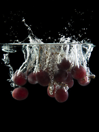 bunch of grapes on black background falling and splashing water, giving a unique feeling of freshness and vitalityの写真素材