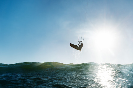 A surfer flying close to the water in the front of the sunの写真素材