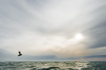 A surfer jumps high in front of a spectacular sunset at the seaの写真素材
