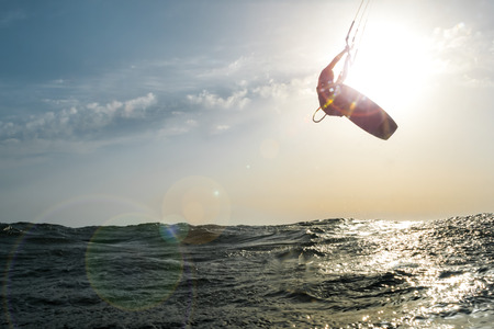 Surfer jumping in front of the sun at sunset over the golden sea, while a beautiful flare enters the cameraの写真素材