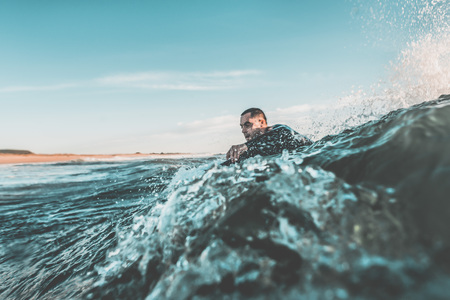 Young man with the water up to the neck trying to catch a wave with his bodyboard among the rough waters of the sea. Extreme water sports and outdoor active lifestyle. Vintage filter with soft styleの写真素材