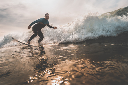 Surfer catching an ocean wave during sunrise. Extreme water sports and outdoor active lifestyle....