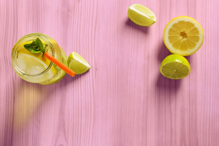 glass jar with homemade lemonade, mint and a cane, on the pink wooden table there are also wedges of lime and lemonの写真素材