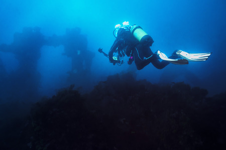 diver with his camera taking a dive through the blue sea towards the wreck. The old remains of the...