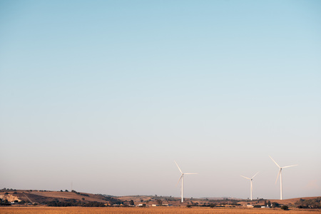 three windmills produce clean energy in a wind farm. They are in a rural environment surrounded by crops and small hills, the sky is clean and clear. Copy spaceの写真素材