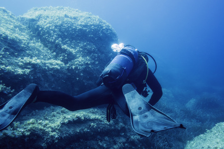 diver submerged near the bottom rocks, the water is blue and turquoise, the stones are covered with...