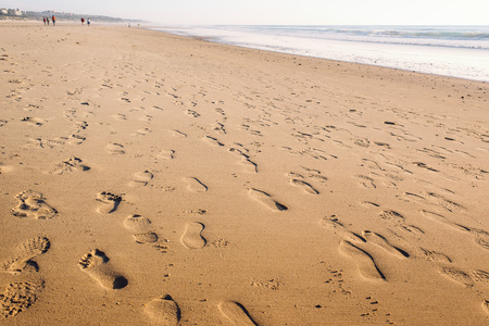footprints in the wet sand of the beach, in the background there are people walking along the shoreの写真素材
