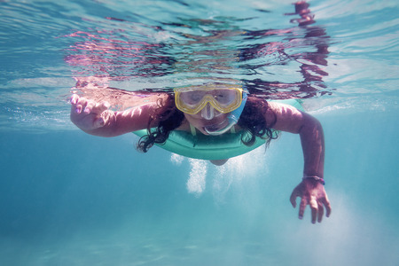 underwater photo of a little girl swimming in the sea with her glasses and snorkel, copy space for textの写真素材