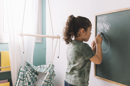 little girl drawing with a chalk on the blackboard at her room at home, copy space for textの写真素材