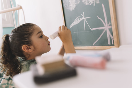 little girl concentrated drawing with a chalk on the blackboard at her room at home, copy space for textの写真素材