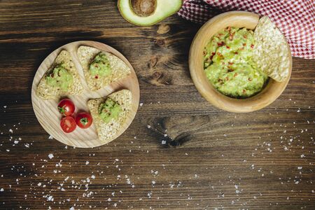 top view of homemade guacamole in a wood bowl with nachos next to an avocado and a kitchen rag, typical mexican healthy vegan cuisine with rustic dark food photo styleの写真素材