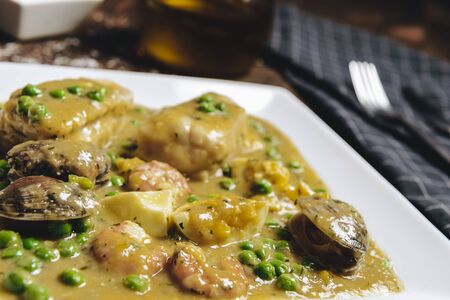 healthy traditional spanish hake dish in green seafood sauce with clams, prawns, green peas and egg,...