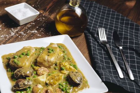 healthy traditional spanish hake dish in green seafood sauce with clams, prawns, green peas and egg, typical mediterranean cuisine with rustic dark food photo styleの写真素材