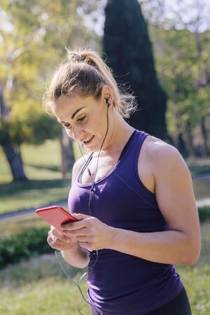 vertical photo of an attractive blonde sports woman setting up her music before her training...
