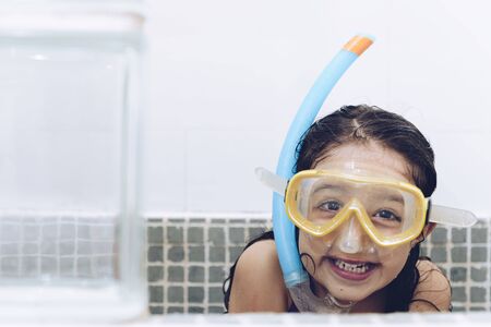 portrait of a happy pretty little girl smiling and having fun with snorkel goggles in the tub while...