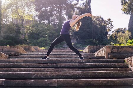 beautiful young woman doing yoga exercises on the stairs of the park, morning workout outdoors, sports and healthy lifestyleの写真素材