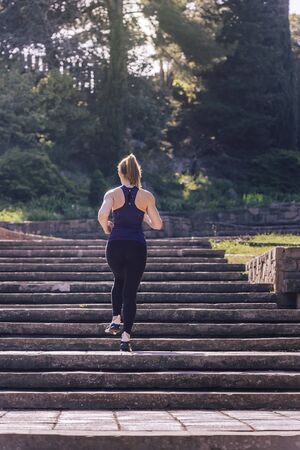 young sporty woman running upstairs in the morning on the stairs of the park, morning workout outdoors, sports and healthy lifestyleの写真素材