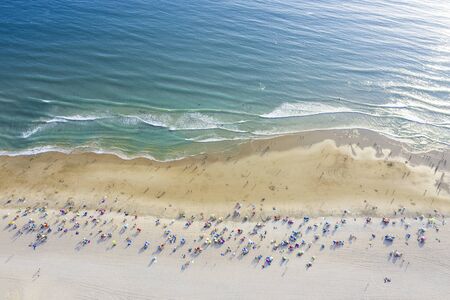 aerial view of sandy beach with colorful umbrellas and lots of tourists swimming in beautiful clear...