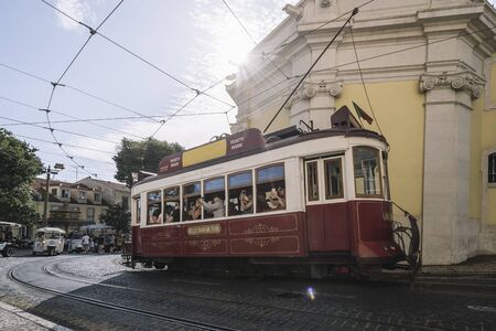 Lisbon, Portugal August, 2019: Typical vintage tourist tram circulating through the cobblestone streets loaded with tourists taking photos with their phonesのeditorial素材