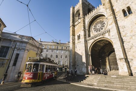 Lisbon, Portugal august, 2019: tourist yellow tram passing by the cobblestone street in front of the cathedral at Alfama districtのeditorial素材