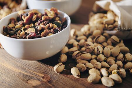 white bowl with mixed nuts, dry fruits and pistachios from a cloth sack on rustic wooden table, healthy food and snack concept, copy space for textの写真素材