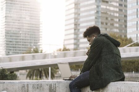modern young man with earphones working on laptop sitting outdoors in the city, lifestyle and technology concept using internet electronic deviceの写真素材