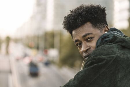 attractive young black african man with green jacket listening music with white earphones, city...