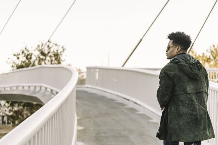 view from behind attractive young black african man with cool casual wear and sunglasses walking on a modern bridge in the city, lifestyle conceptの写真素材