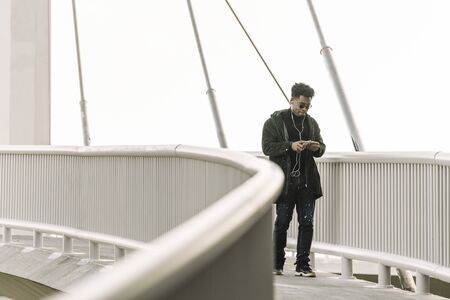 black man walks around looking at his smartphone while listen music in earphones in the city,...