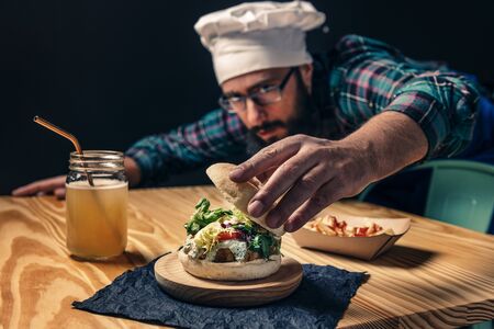 chef finishing up his vegan burger with lettuce tomato and sauce, fries with ketchup and healthy drink on a wooden table, vegetarian food and foodie lifestyle concept, selective focusの写真素材