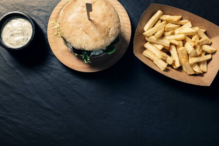 gourmet burger with lettuce on a slate background with french fries in a cardboard tray and a jar of...
