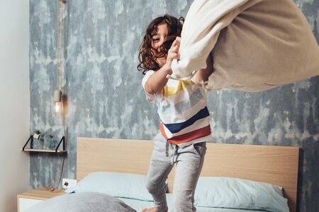 funny little girl throwing a cushion standing on her parents bed, home lifestyle concept and happy childhoodの写真素材