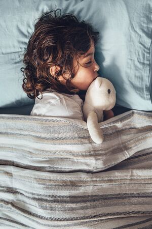 adorable little girl sleeping in bed hugging her teddy bear, happy childhood and healthy rest concept, vertical photoの写真素材
