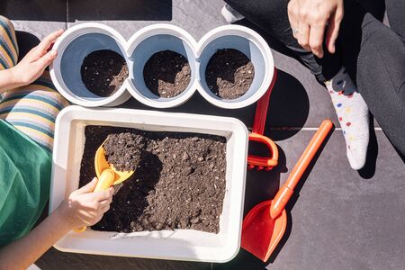 top view of the hands of a child and her mother in the balcony of home preparing dirt in pots for...