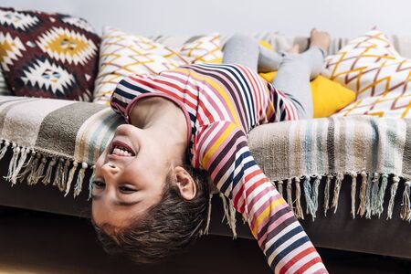 funny little girl laughs happy lying on the couch, concept of children at home and home lifestyleの写真素材