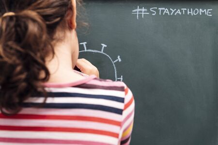 child drawing a coronavirus on a blackboard with the message, stay at home, concept of kids in quarantine, copy space for textの写真素材