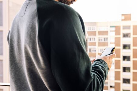unrecognizable man checking his smart phone on the balcony of his house, concept of communication...