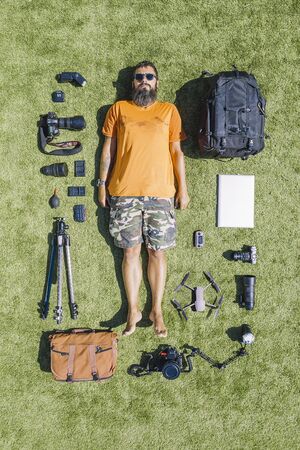 flat lay of a photographer and all his equipment of cameras, lenses, backpack, tripod on a grass...