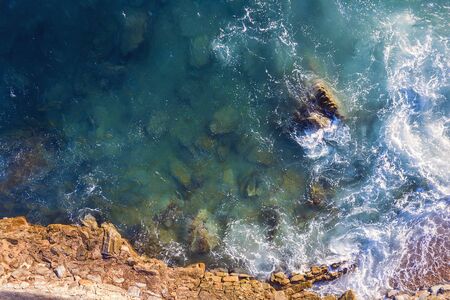 top view of sea waves hitting on the seashore of the rocky coast with spray and foam, power of the...