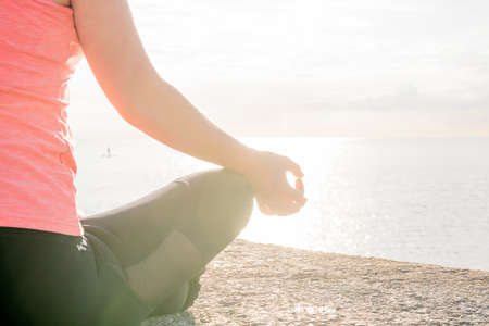 hand of an unrecognizable woman practicing yoga at dawn sitting in the lotus position in front of...