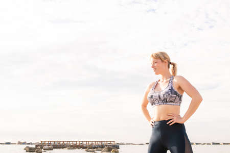 beautiful blonde sports woman posing powerfully on the beach with her hands on her hips, healthy lifestyle and sports concept, text copyの写真素材