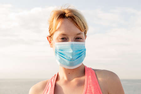 portrait of a beautiful blonde woman with a protective mask with the sky in the background, concept of prevention and health careの写真素材