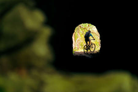 cyclist with backpack and mountain bike leaving at the end of a tunnel, concept of sport and healthy lifestyle in nature, copy space for textの写真素材