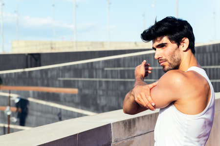 handsome sportsman stretching his shoulder and back muscles, concept of urban sport and healthy lifestyle, copy space for textの写真素材