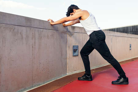 unrecognizable sportsman stretching legs on a concrete wall, concept of urban sport and healthy...